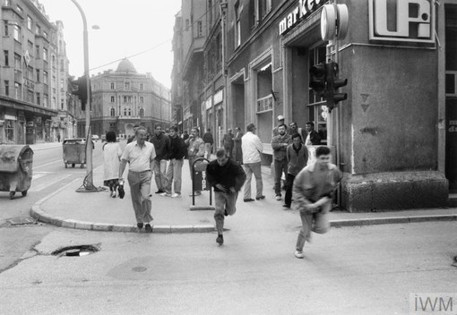 MEN RUN across the junction of a side street with Maršala Tita, a main thoroughfare in Sarajevo. Serbian snipers were known to be positioned at the end of the side street and would fire on civilians and military personnel at any time, Image by Kevin Weaver, June 1992. Copyright © IWM. IWM catalogue reference HU 75060, Original source https://www.iwm.org.uk/collections/item/object/205020574.