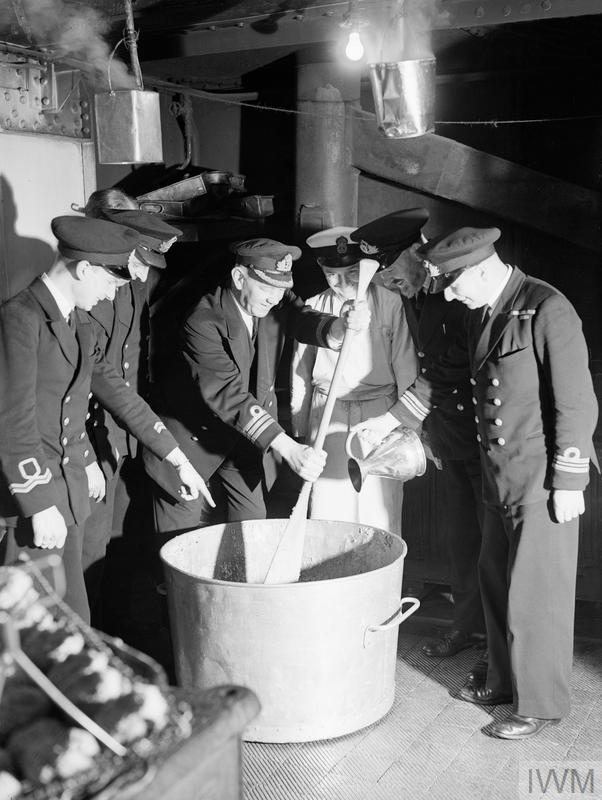 THE COMMANDER of a destroyer depot ship in the Home Fleet at Scapa Flow stirs a traditional Christmas pudding, while the First Lieutenant adds a tot of rum. Although the wartime caption does not mention the ship, this is possibly HMS Tyne. The ship served as the flagship of Rear-Admiral R.L. Burnett, CB, DSO, OBE, RN while Destroyer Flotillas of the Home Fleet/ He would later be appointed Flag Officer of the 10th Cruiser Squadron, with HMS Belfast as his flagship. Image Copyright: © IWM. IWM catalogue reference A 13317. Original Source: http://www.iwm.org.uk/collections/item/object/205186123